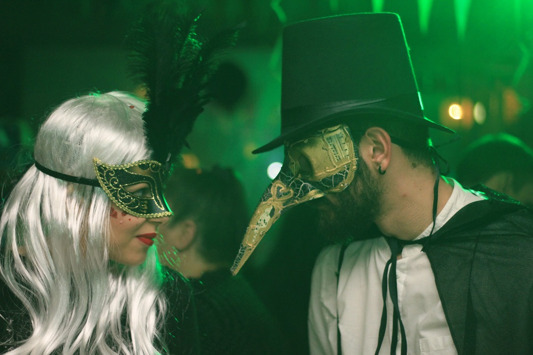 Two adults look at each other in costume; both wearing masks.