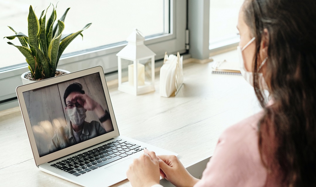 A woman wears a mask in a cafe, on a videoconference with a man also wearing a mask