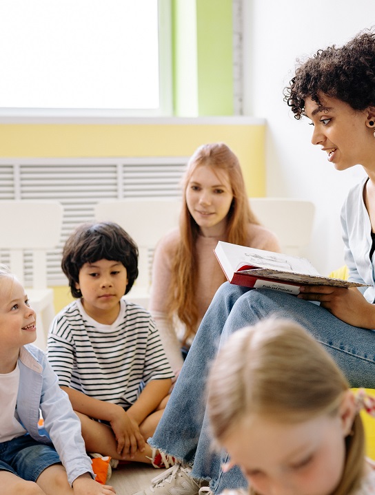A female child health nurse reads to a group of children in a setting which could be used to detect autism in preschoolers