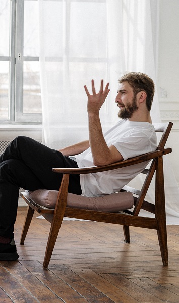 A white man sits in a chair, using body language to communicate with someone that isn't pictured. It represents a man seeking an autism diagnosis in adults.