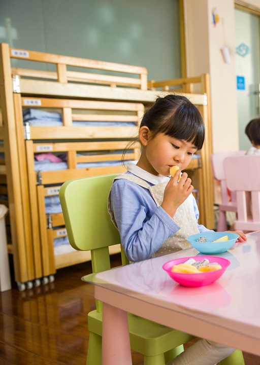 Managing selective eating for autsitics: A young toddler sits at the same table as the child in the previous image. They are putting fresh food to their lips as if deciding whether to eat it or not.