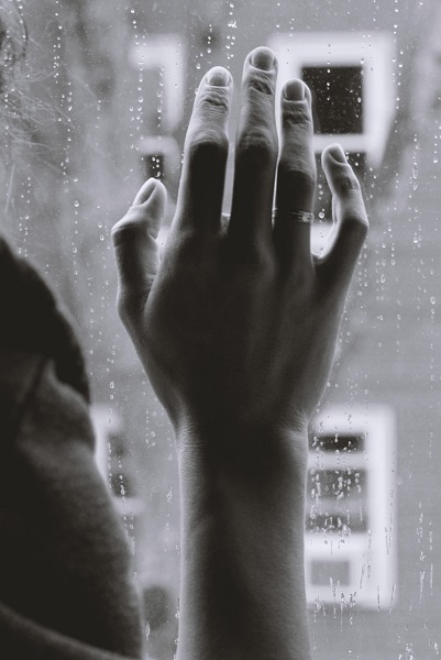 Loneliness in autistic adults: a black and white image of a womans hand against a window pane.